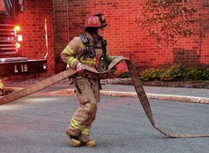 Firefighter carrying a fire house at scene of fire
